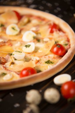 Kiraz domatesli pizzanın yarısı, pesto sosu, parmesan peyniri, peynir, tavuk filetosu, domuz pastırması, bıldırcın yumurtası, ahşap zemin üzerinde mozzarella peyniri deniz tuzu ve malzemelerle birlikte. Kesilmemiş pizzaya yaklaş