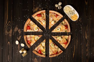 Domatesli pizza, pesto sosu, pastırma, bıldırcın yumurtası, mozzarella ve ahşap zemin üzerinde deniz tuzu ve malzemelerle parmesan peyniri. Yemeklerin yanında üç çeşit peynir ve bıldırcın yumurtası.