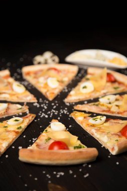 Domatesli dilimlenmiş pizza, pesto sosu, pastırma, mozzarella ve parmesan peyniri ahşap tahtada deniz tuzu ve malzemelerle. Tabakta üç çeşit peynir ve arka planda üç bıldırcın yumurtası.