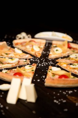 Domatesli pizza, pesto sosu, pastırma, bıldırcın yumurtası, mozzarella ve ahşap arka planda deniz tuzu ve malzemelerle parmesan peyniri. Yemeklerin yanında üç çeşit peynir ve bıldırcın yumurtası.