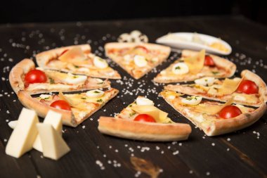 Domatesli pizza, pesto sosu, pastırma, bıldırcın yumurtası, mozzarella ve ahşap zemin üzerinde deniz tuzu ve malzemelerle parmesan peyniri. Pizza parçalarının yanında üç çeşit peynir ve bıldırcın yumurtası.