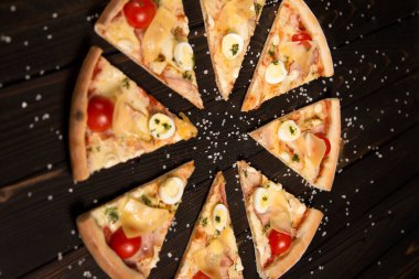 Domatesli pizza, pesto sosu, pastırma, bıldırcın yumurtası, mozzarella ve parmesan peyniri ile ahşap tahta arka planda deniz tuzu ve malzemelerle. Kırsal yemek.