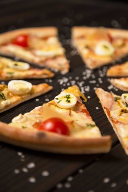 Vişneli domates, pesto sosu, pastırma, bıldırcın yumurtası, mozzarella ve parmesan peyniri ile ahşap tahta zeminde deniz tuzu ve malzemelerle birlikte pizza dilimini kapat..