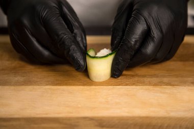 Japon Gunkan Sake Green. Salatalığa sarılmış pirinç. Şef restoranda Pan Asya yemeği hazırlıyor. Şefin elleri siyah eldivenli. Tahta kesme tahtasındaki suşi pişirme işlemini kapat