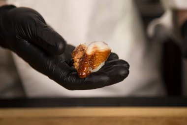 Şef geleneksel Japon suşi nigiri 'sini yılan balığıyla tutuyor. Şefin elleri siyah koruma eldivenlerinde. Unagi kapat. Pan Asya deniz ürünleri yemeği hazırlanıyor. Restoran yemeği hazırlama işlemi devam ediyor..