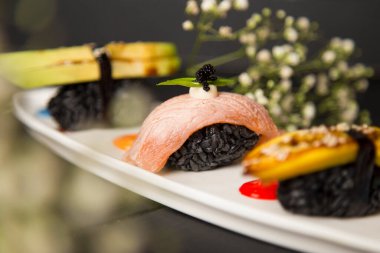 Japon nigiri seti. Somon Sake Tataki 'ye siyah pirinç, mayonez, uçan balık yumurtası (Tobiko havyarı) ekleyin. Arka planda çiçekler olan dekore edilmiş yemek tabağı. Asya restoran menüsü