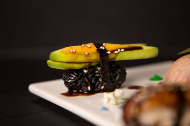 Avokado, susam tohumu ve Unagi soslu Japon Nigiri Sushi renkli çiçek ve boyalarla süslenmiş beyaz tabağa odaklanmış. Yemek dekorasyonu. Pan Asya deniz ürünleri restoran menüsü mutfak konsepti