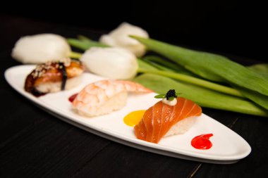 Japon Nigiri Sake Suşi seti ve somon, Nigiri Ebi 'nin yanında karidesli ve Unagi ile yılan balığı. Renkli yemek süslemeleri, beyaz lalelerin yanındaki tabakta boya lekeleri. Asya restoran menüsü