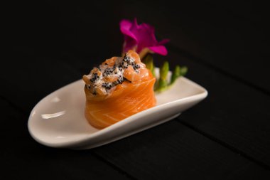 Çiçekle süslenmiş beyaz tabakta uçan balık yumurtası ile birlikte somon balıklı suşi rulosu. Taze somonlu Japon Gunkan Sake, tobiko havyarı ve Philadelphia krem peyniri. Pan Asya deniz ürünleri restoran menüsü