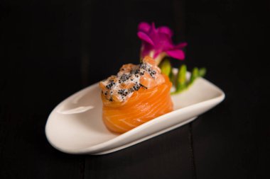 Taze somonlu Japon Gunkan suşisi ve çiçeklerle süslenmiş beyaz tabakta Tobico havyarı. Koyu ahşap arka planda Asya geleneksel yemeği. Pan Asya restoran menüsü. Deniz mahsulleri suşi rulosu.