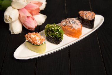 Hiyashi wakame chuka maki rulo ve salatalık içinde somon sakesi ile Japon Gunkan setleri yakında beyaz tabağa odaklanıyor. Ahşap tahtada çiçekli Asya geleneksel yemeği. Lezzetli restoran menüsü