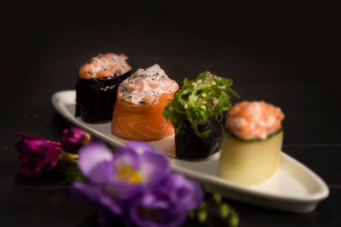 Beyaz tabağa odaklanmış Sake somonlu bir grup Japon Gunkan. Koyu ahşap tahtada çiçekli somon balıklı Asya yemeği. Suşi restoranı menüsü kapanıyor. Pahalı yemekler.