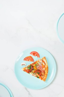 Domates, salam, tavuk filetosu, jambon, şampiyon ve yeşil otlu et pizzası. Pastel mavi tabakta malzemeli pizza, beyaz mermer arka plan, servis tabaklarının parçaları..