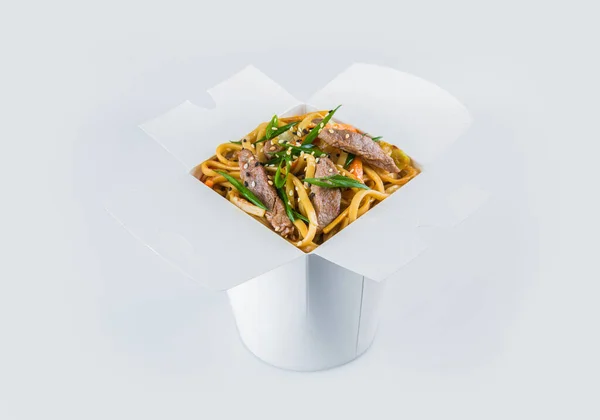 Biftek fileto, sebze, soya sosu ve taze soğan soğanı ile birlikte beyaz karton paket servis kutusunda yalıtılmış Asya Udon Eriştesi. Yemek paketi ve içinde yemek hazır.