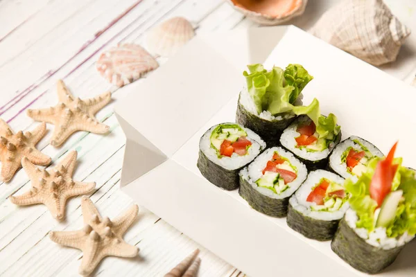 Japon Futomaki Sushi Roll parçaları karton teslimat kutusunda. Domates, salatalık, avokado, paprika, ahşap tahtada salata karışımı deniz kabuğu ve arka planda yıldızlar olan Asya sebzeli Maki rulosu.