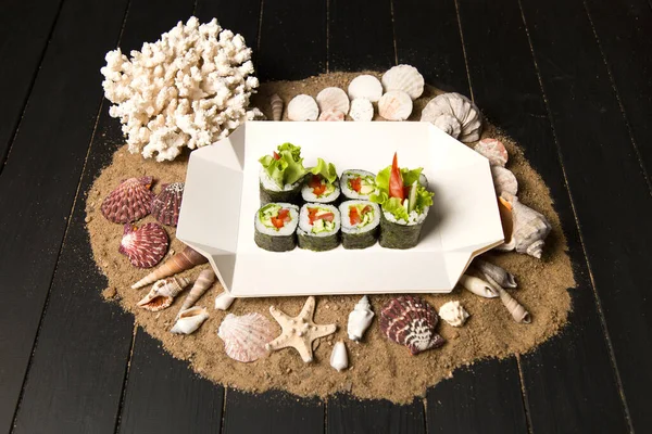 Japon Futomaki Sushi Roll parçaları karton teslimat kutusunda. Domates, salatalık, avokado, paprika, ahşap tahtada salata karışımı okyanus mercanı, deniz kabuğu ve kumdaki yıldızlar.