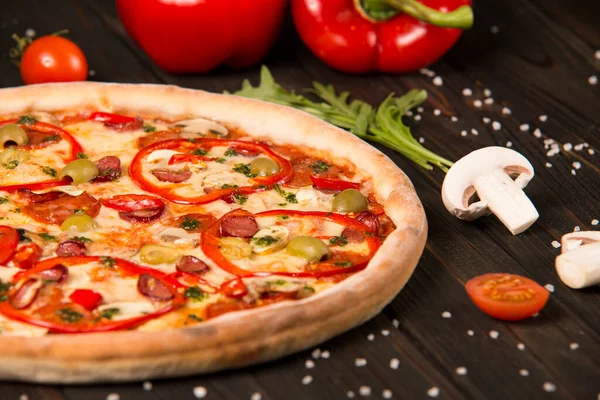 Biberli pizzanın bir kısmı, şampiyonlar, kiraz domatesleri, deniz tuzu ve ahşap arka planda otlar. Kesilmemiş pizzaya yaklaş