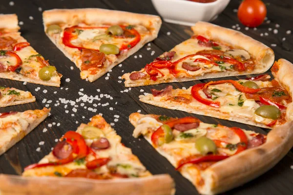 Lezzetli pizza dilimleri. Yanında dolmalık biber, zeytin, sosis, mozzarella peyniri, pepperoni, salam, acı biber, ahşap zemin üzerinde şampiyonlar ve odakta deniz tuzu..