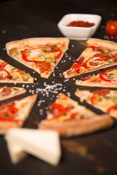 Dilimlenmiş pizzayı dolma biber, zeytin, sosis, mozzarella peyniri, pepperoni, salam, biber, ahşap tahtada şampiyonlar ve arka planda deniz tuzu ve malzemeleriyle kapatın..