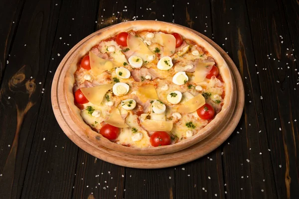 Kiraz domatesli pizza, pesto sosu, parmesan peyniri, tavuk filetosu, domuz pastırması, bıldırcın yumurtası ahşap zeminde mozzarella peyniri ve deniz tuzu. Tahtada dilimlenmemiş lezzetli pizza.