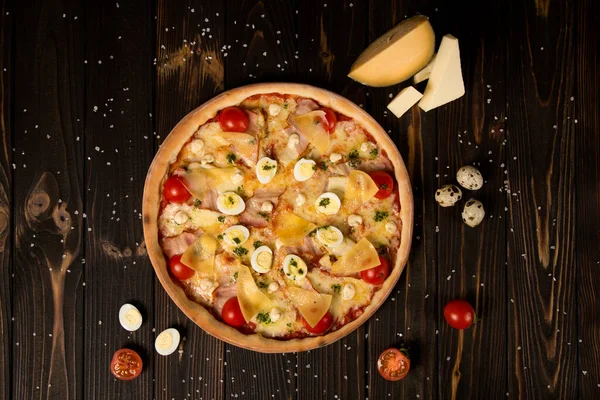 Kiraz domatesli pizza, pesto sosu, parmesan peyniri, tavuk filetosu, domuz pastırması, bıldırcın yumurtası, ahşap zemin üzerinde mozzarella peyniri ve deniz tuzu ve malzemesi. Lezzetli kesilmemiş pizza.