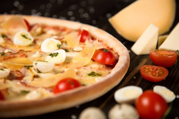 Kiraz domatesli pizza, pesto sosu, parmesan peyniri, tavuk filetosu, domuz pastırması, bıldırcın yumurtası, ahşap zemin üzerinde mozzarella peyniri deniz tuzu ve malzemeleriyle. Kesilmemiş pizzaya yaklaş