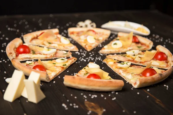 Domatesli pizza, pesto sosu, pastırma, bıldırcın yumurtası, mozzarella ve ahşap zemin üzerinde deniz tuzu ve malzemelerle parmesan peyniri. Pizza parçalarının yanında üç çeşit peynir ve bıldırcın yumurtası.