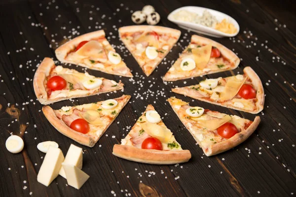 Domatesli pizza, pesto sosu, pastırma, bıldırcın yumurtası, mozzarella ve ahşap arka planda deniz tuzu ve malzemelerle parmesan peyniri. Yemeklerin yanında üç çeşit peynir ve bıldırcın yumurtası.