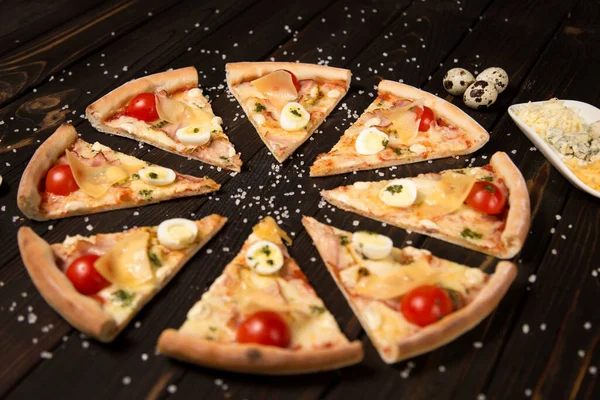 Domatesli dilimlenmiş pizza, pesto sosu, pastırma, mozzarella ve ahşap zemin üzerinde parmesan peyniri deniz tuzu ve malzemelerle birlikte. Tabakta üç çeşit peynir ve pizza parçalarının yanında üç bıldırcın yumurtası.