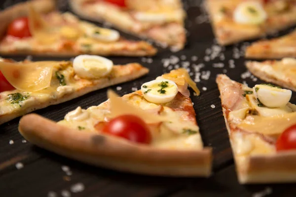 Vişneli domates, pesto sosu, pastırma, bıldırcın yumurtası, mozzarella ve parmesan peyniri ile ahşap tahta zeminde deniz tuzu ve malzemelerle birlikte pizza dilimini kapat. Odaklanan tek bileşen