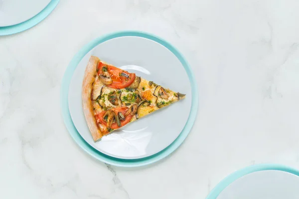 Slice of Vegan vegetable pizza. Food on pastel turquoise and gray serving plates. tableware on marble background. Dish with tomatoes, eggplant, champignons, Mozzarella cheese and basil pesto sauce.