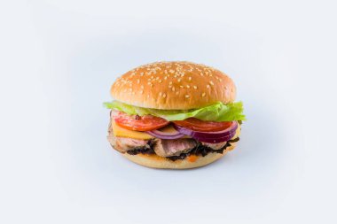 Sebzeli domuz burger ve susamlı peynirli çörek. Arka planda taze salata yaprakları, domatesler, İspanyol soğanları ve soslu et burgeri. Gıda İzolasyon Restoran menüsü