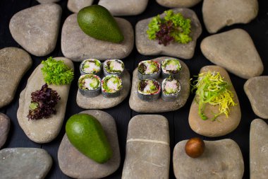 Japon suşisini pirinçsiz, deniz taşları üzerinde servis edilen daikon turpuna sarılmış yengeç etli (yengeç çubukları) Japon suşisiyle kapatın. Arka plandaki malzemeler. Avokado ve salata karışımı. Yanında pirinç yemeği yok.