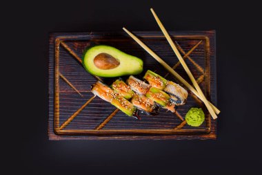 Japon suşi rulosu, siyah pirinç, unagi yılan balığı, avakado, wasabi sosu, susam tohumu, çubuk ve ahşap tahtada avokado meyvesinin yarısı. Koyu arkaplanda Pan Asya yemeği