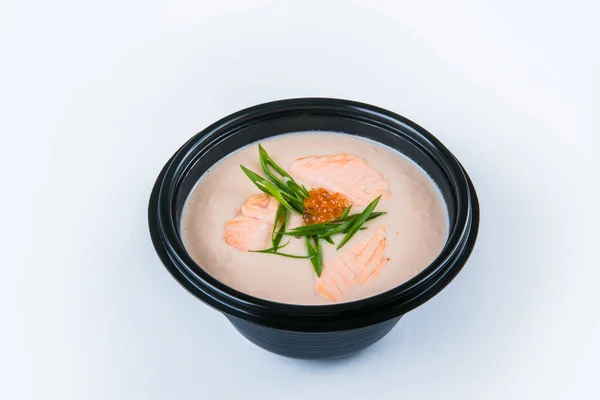 Salmon cream soup with salmon fillet pieces, red caviar and spring onion scallions served in plastic delivery bowl. Dish isolated on gray background. Asian first dish in black plate. Food isolation — Stock Image Salmon Cream Soup Salmon Fillet Pieces Red Caviar Spring Onion Royalty Free Stock Photos