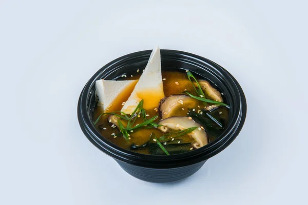 Asian traditional Miso Soup with salmon, Shiitake mushrooms, Tofu cheese, Hiyashi Wakame seaweed and spring onion scallions served in plastic delivery bowl, isolated on gray background — Stock Image Asian Traditional Miso Soup Salmon Shiitake Mushrooms Tofu Cheese Hiyashi Royalty Free Stock Images