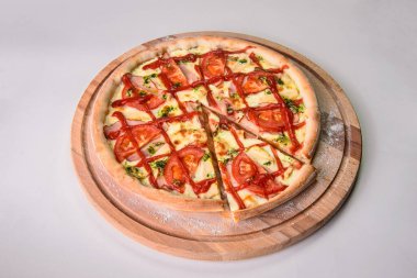 Kesilmemiş pizzanın tamamı ahşap kesim tahtasının üzerinde. Arkaplanda un ile servis ediliyor. Restoran fast food menüsü izolasyonu. Erimiş peynir, domates ve bbq soslu bir dilim et pizzası.