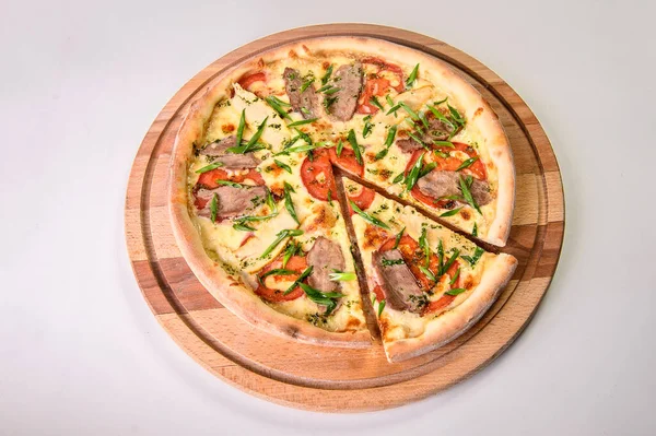 Kesilmemiş pizza, et, domates ve taze soğanlı soğanlı yeşil soğanlı arka planda izole edilmiş tahta kesme tahtası. Restoran fast food menüsü izolasyonu. Erimiş peynirli bir dilim et pizzası.
