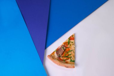 Domatesli, peynirli ve taze soğanlı leziz bir dilim pizza mavi renkli kağıt parçalarının yanında. Tek parça İtalyan pizzası..