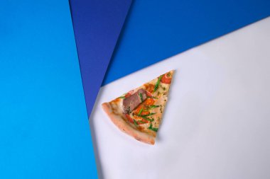 Domatesli, peynirli ve taze soğanlı leziz et pizzasını açık arka planda mavi renkli kağıt parçalarının yanına koyun. Tek parça İtalyan pizzası..