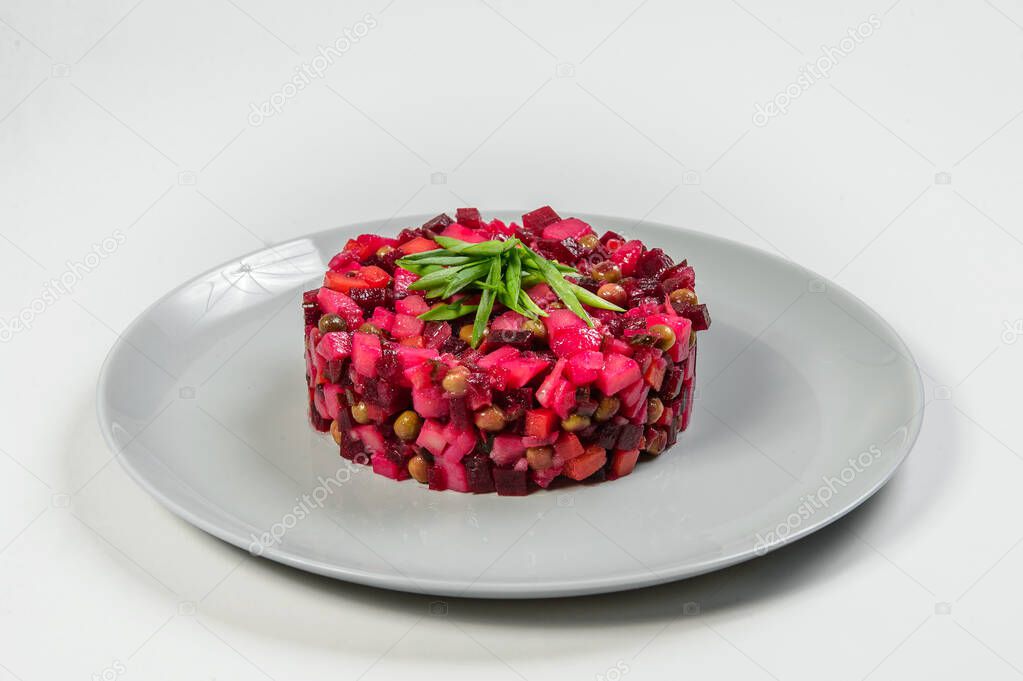 Traditional Russian salad vinaigrette served with spring onion scallions in culinary ring on serving plate isolated on gray background. Vegetable beetroot Ukrainian salad. 