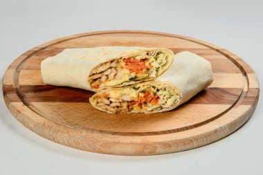 Izgara et shawarma rulosu ahşap tabakta servis ediliyor, arka planda izole edilmiş. Tavuk fileto jiroskopu, salatalık turşusu, lahanaya sarılmış havuç. Dandik Doğu Arap sokak yemekleri sandviçi