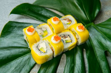 Japon suşi rulosu mango, avokado, unagi yılan balığı ve Philadelphia peyniri antrakit arka planda yeşil tropikal canavar yaprağında servis edilir. Pan Asya menüsünde egzotik bitki yaprağına ekmek parçaları