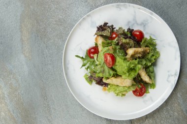 Tavuklu Tempura Salatası beyaz mermer tabakta servis edilir. Kızarmış tavuk şeritli et tabağı, salata karışımı ve antrasit arkaplanlı vişneli domates. Metin kopyalama alanı