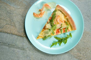 Tabağındaki malzemelerle birlikte bir dilim tavuk pizzası. Antrasit taşından arka plandaki fast food yemeğinin en üst görüntüsü. Bir parça karidesli deniz ürünleri pizzası, taze roka yaprakları ve dilimlenmiş parmesan peyniri.