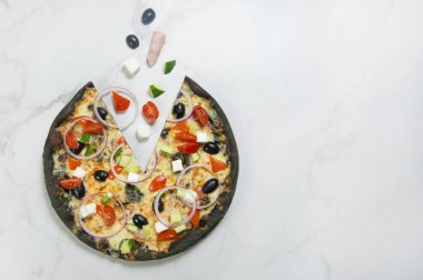 Beyaz mermer arka planda sebzeli İtalyan etli siyah hamurlu pizza: kirazlı domates, salatalık, zeytin, Feta peyniri. Uçan yiyecek konsepti. Soğan halkalarıyla servis edilir. Boşluğu kopyala