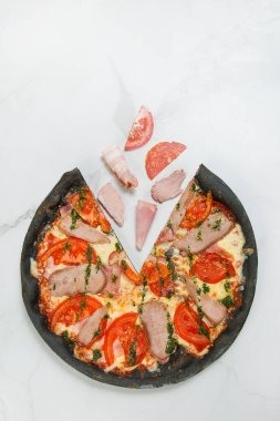 Beyaz mermer arka planda İtalyan eti siyah hamurlu pizza: domates dilimleri, jambon, pastırma, salam, domuz eti ve sığır eti. Uçan yiyecek konsepti. Pesto soslu pizza. Metin uzayı, kopyalama alanı