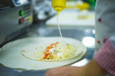Şef profesyonel restoran mutfağında jiroskop yapıyor. Lavaş ekmeği (pita) tavuk, havuç ve peynirli. Shawarma Pişirme İşlemi. Şef mayonez dolduruyor. 