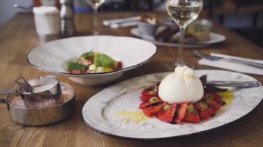 Domates ve fesleğenli burrata. Restoranın masasında güzel bir tabak ve bir bardak şarap duruyor. Restoranda servis edilen Burrata tabağı. Bir tabak şarapla güzel bir kompozisyon..