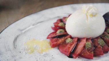 Domates ve fesleğenli burrata. Restoranın masasında güzel bir tabak ve bir bardak şarap duruyor. Restoranda servis edilen Burrata tabağı. Bir tabak şarapla güzel bir kompozisyon..